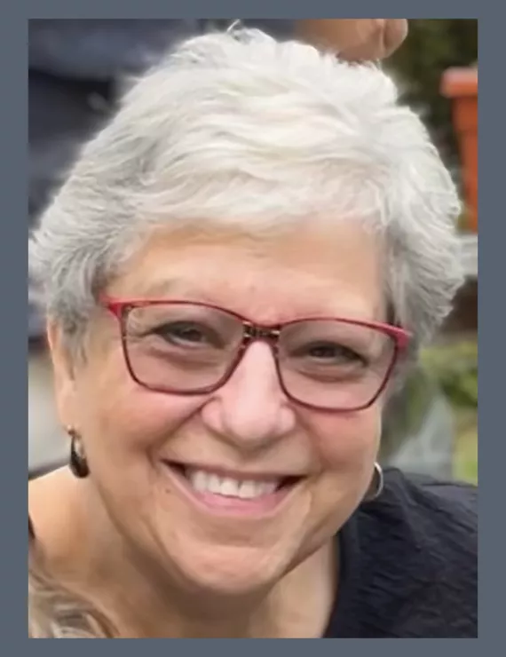 Image of gray haired woman who is smiling, wearing red eyeglasses