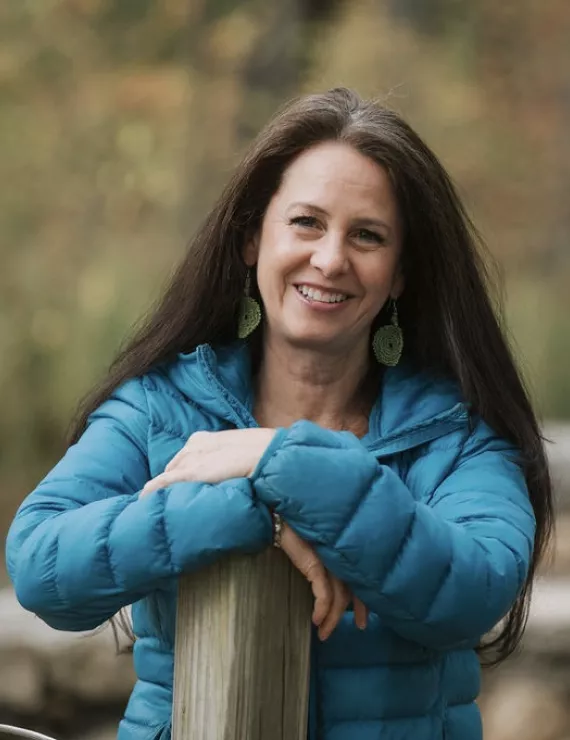 Photo of caucasian female, long brown hair, smiling, blue jacket, outdoors.