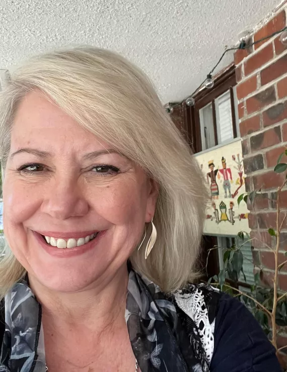 60 yo woman with blonde/gray hair. smiling on sun porch 