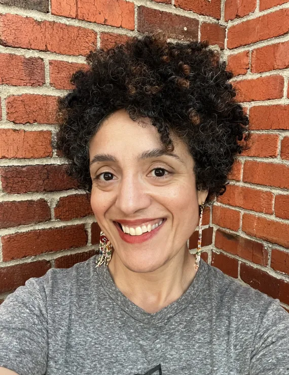 Multiracial BIPOC IFS Therapist in Oakland, CA - Shirin Shoai, MFT smiling in front of a brick building