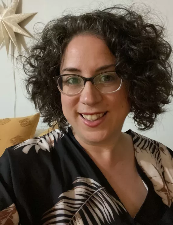 Picture of a woman with a short brown curly haired bob, glasses and a smile