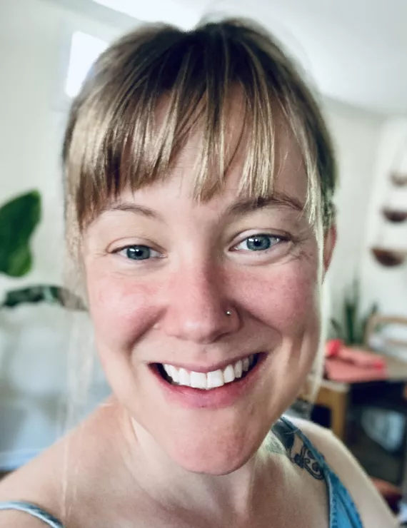 A close up head shot of Caitlin, a white woman with bangs, smiling at the camera.