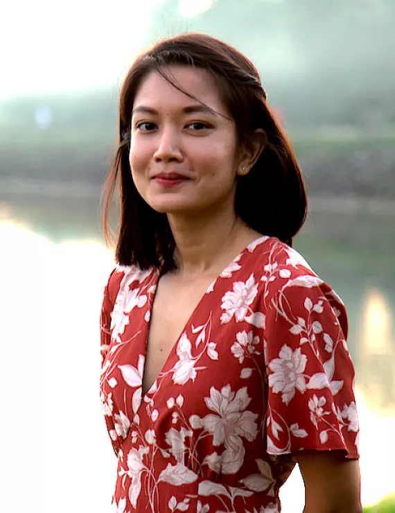 Headshot of a woman wearing orange, flowery dress against a blurred backdrop of nature
