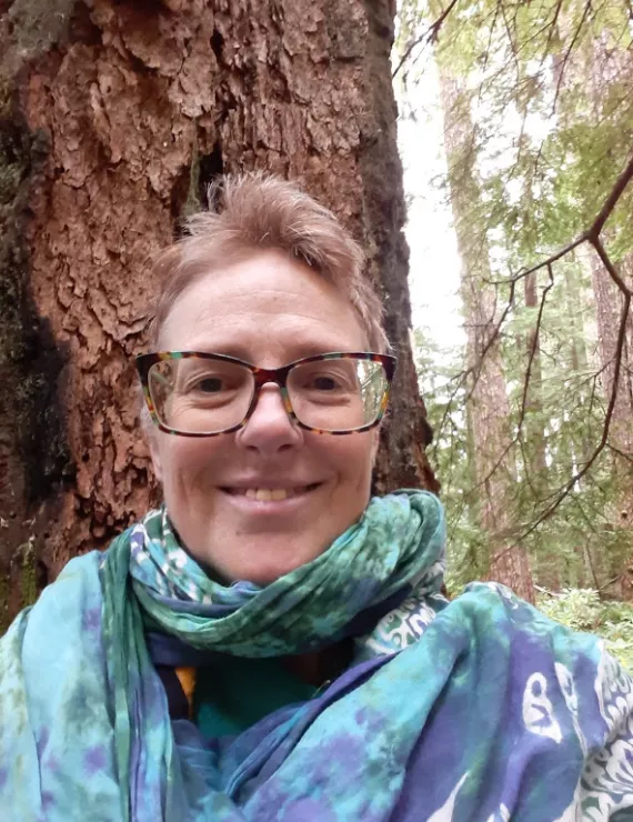 Smiling middle aged white woman with glasses standing in front of a big tree