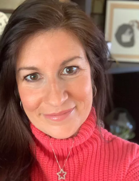 image of face with bookcase in background, red turtleneck sweater and star pendant, with long dark hair