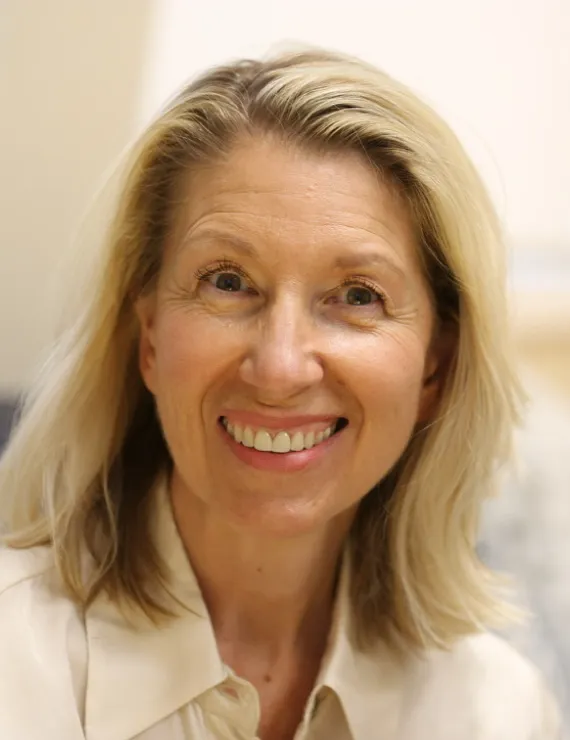 Smiling blonde woman with cream shirt, with office in the background