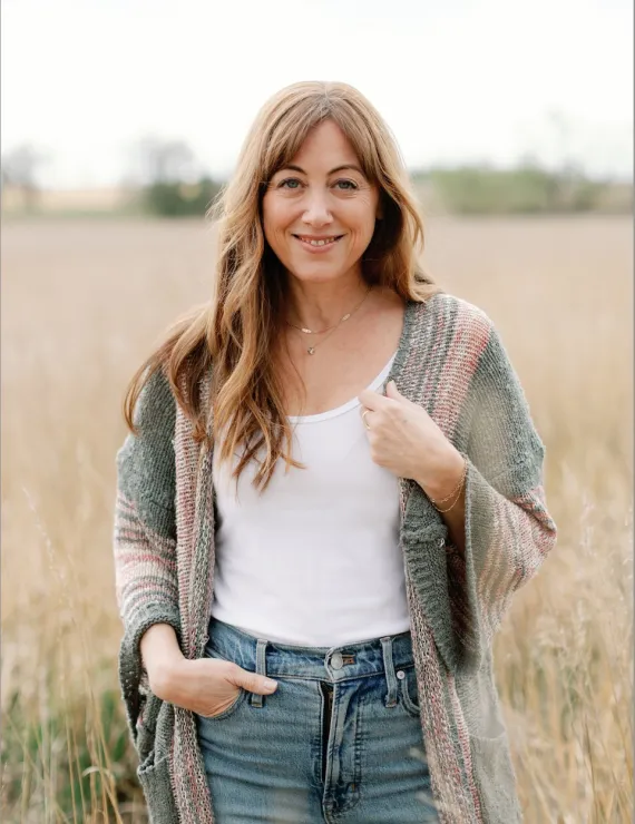 Tara standing in a field wearing a sweater and jeans