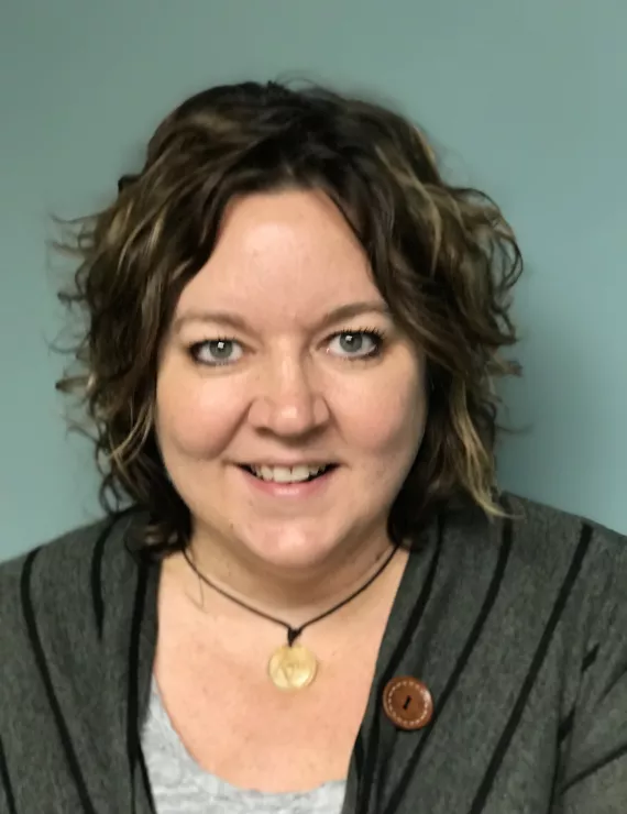 Therapist with wavy hair, wearing a casual sweater and a necklace. 