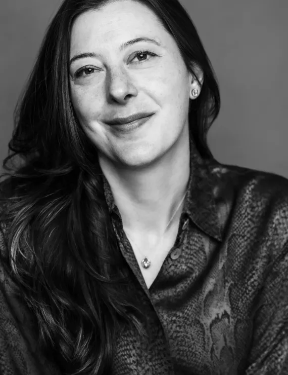 Jennifer has long hair and is in a silk button-up blouse. The photo is black and white. Jennifer is smiling slightly.