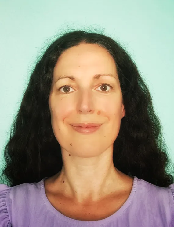 Portrait of a woman with long curly hair, facing the camera and smiling gently.
