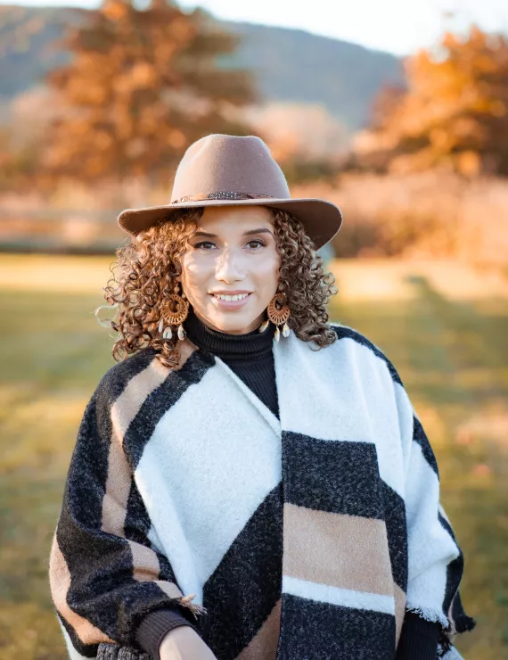 Natalie headshot, wearing a hat in a natural autumn background