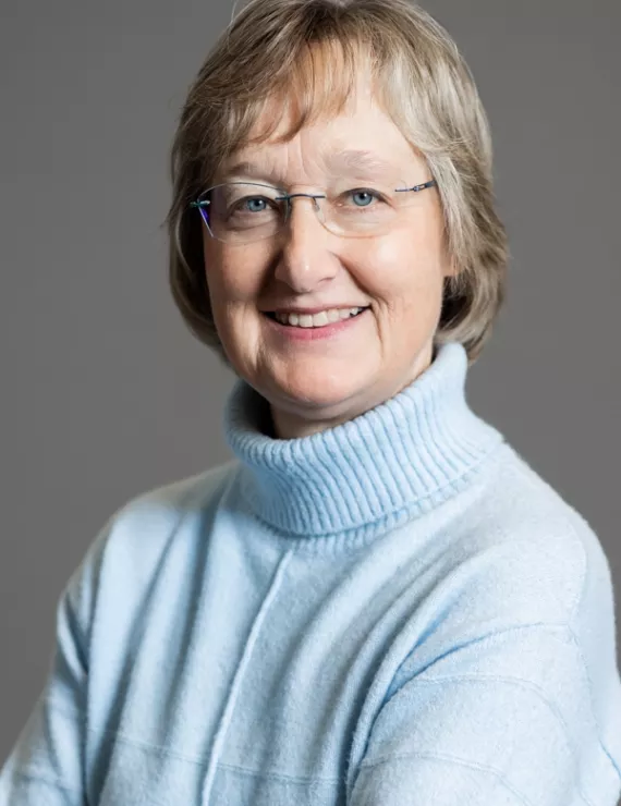 white woman with short blond hair and glasses wearing a light blue turtleneck sweater